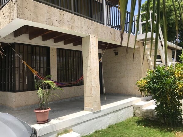 A two-story building with a balcony, a hammock, and potted plants.
