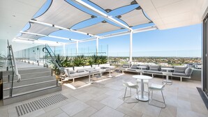 A modern outdoor lounge area with a glass balustrade, tiered seating, and a clear view of the cityscape. - Vibe Hotel Subiaco Perth (Subiaco)