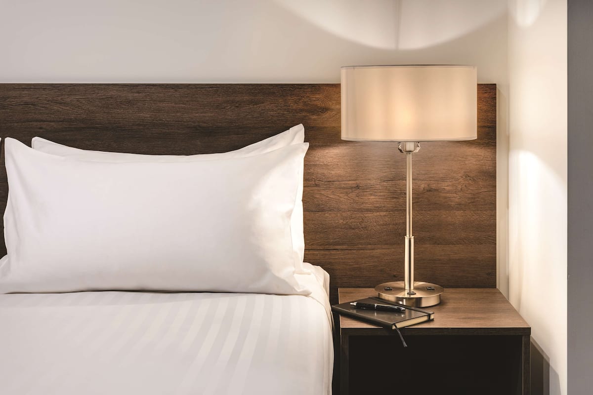 A neatly made bed with white pillows and a striped bedspread, a bedside table with a lamp, and a wooden headboard.