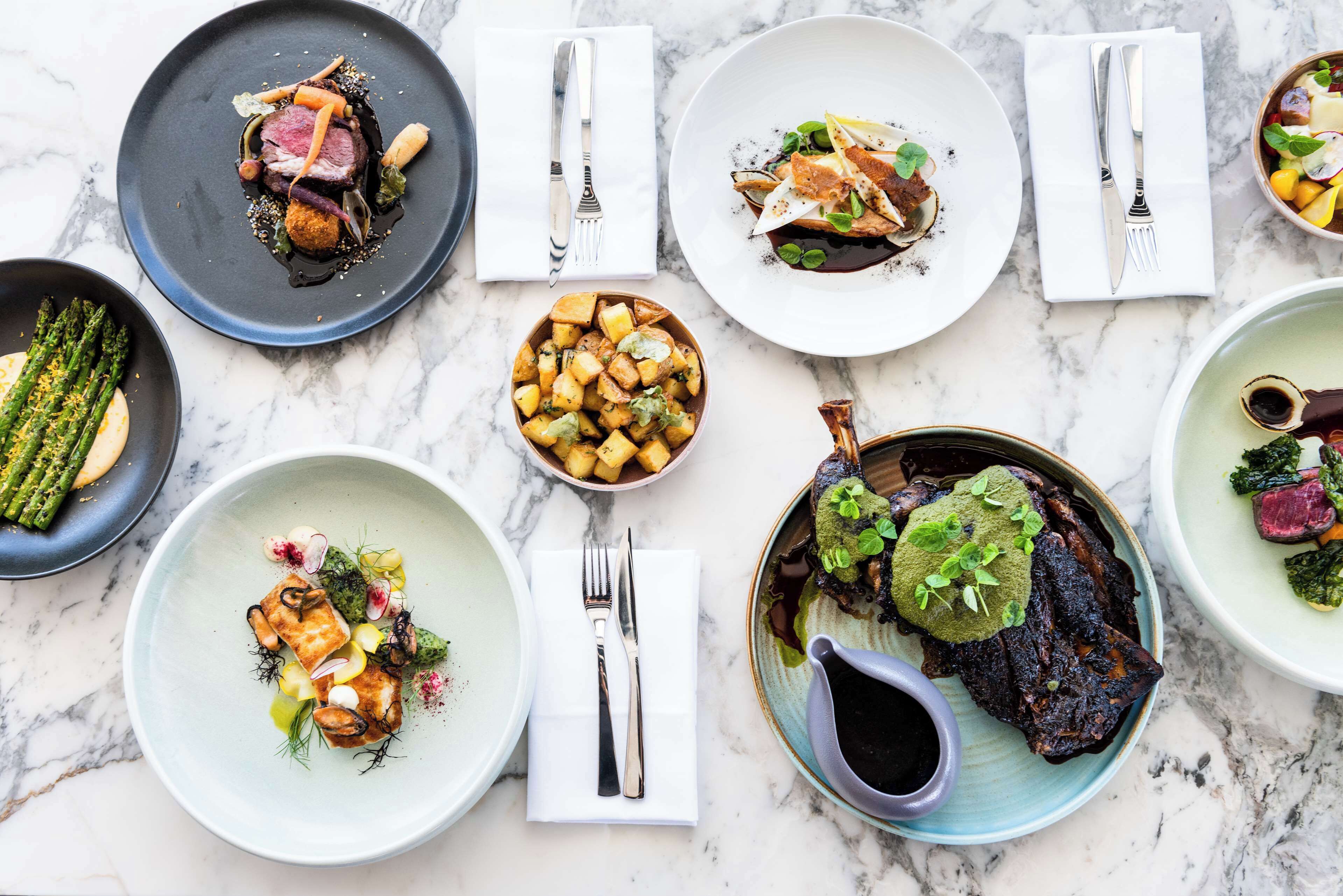 A variety of dishes on a marble table, each with different garnishes and sauces.