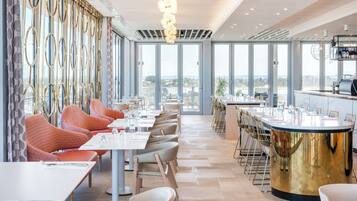 Un restaurante moderno con un amplio comedor, ventanas grandes y una barra con mostrador dorado.