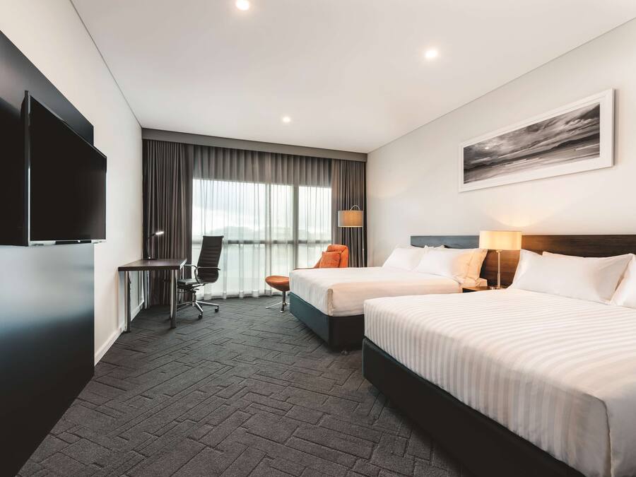 A hotel room with two beds, a desk, a chair, a television, and a window with curtains.