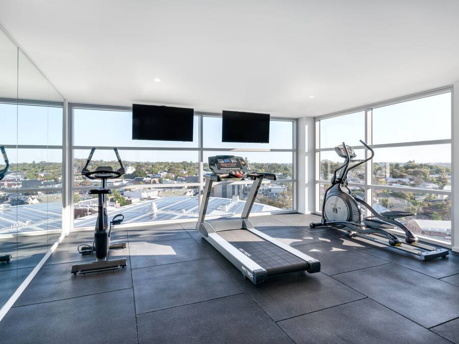 Une salle de sport équipée de tapis de course, d’un vélo elliptique et d’un vélo d’appartement, avec de grandes fenêtres offrant une vue sur la ville.