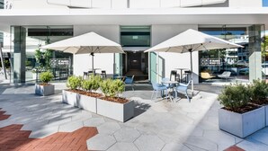 An outdoor seating area with white umbrellas, planters with greenery, and a modern building facade with glass windows and signage for "ST MARKS ROAD CO." - Vibe Hotel Subiaco Perth (Subiaco)