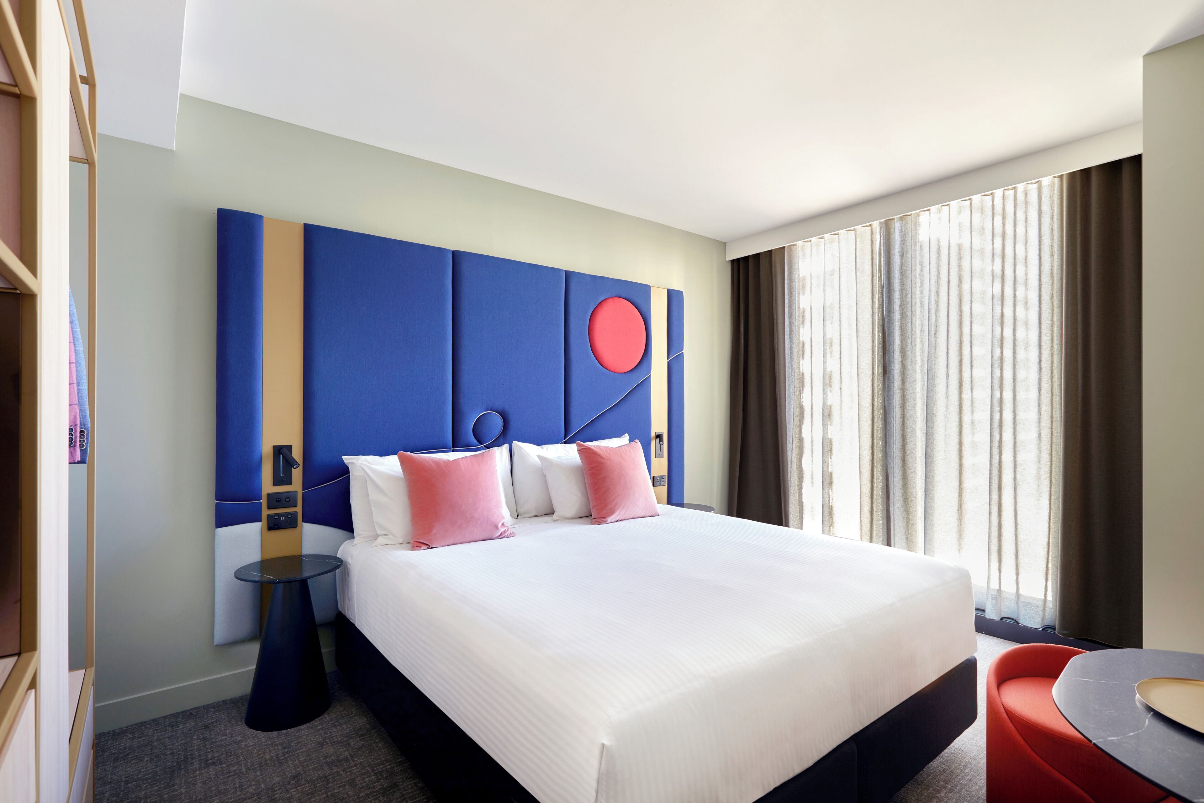 A hotel room with a large bed, a bedside table, a round table, and a view of the outdoors.