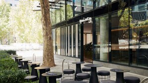 Outdoor seating with round tables and chairs, a tree, and a building with large windows. - Quincy Hotel Melbourne (Melbourne)