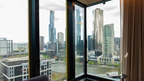 A room with a large window offering a view of a cityscape with modern buildings and a river. - Quincy Hotel Melbourne (Melbourne)