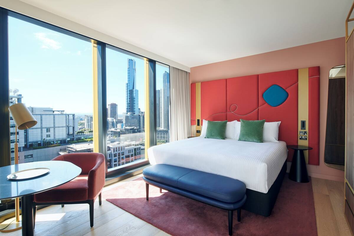 Habitación de hotel con un ventanal grande, una cama, un escritorio y una silla.