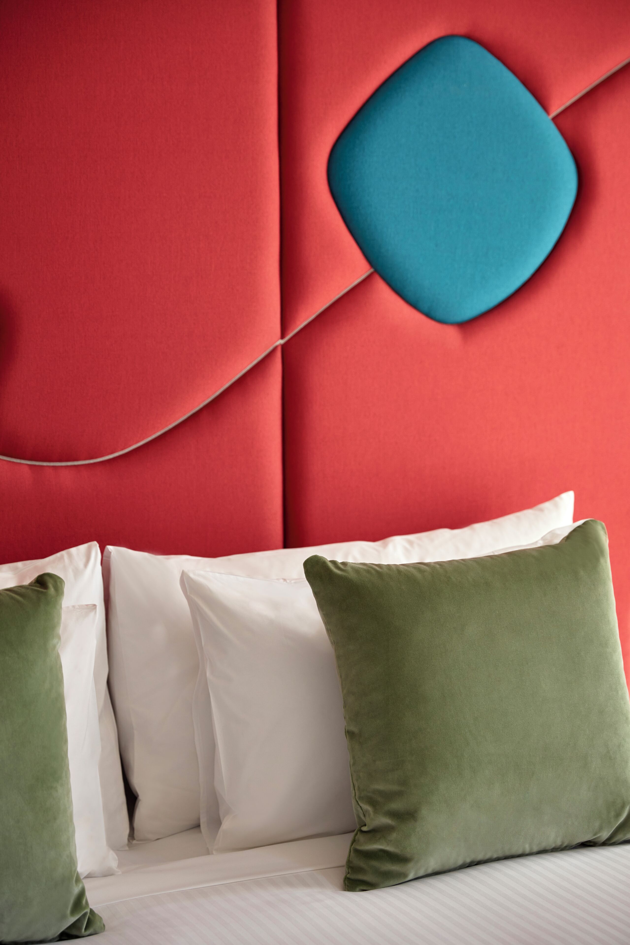 A bed with white and green pillows, a red headboard with a blue accent, and a white wall.