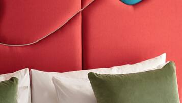 A bed with white and green pillows, a red headboard with a blue accent, and a white wall.