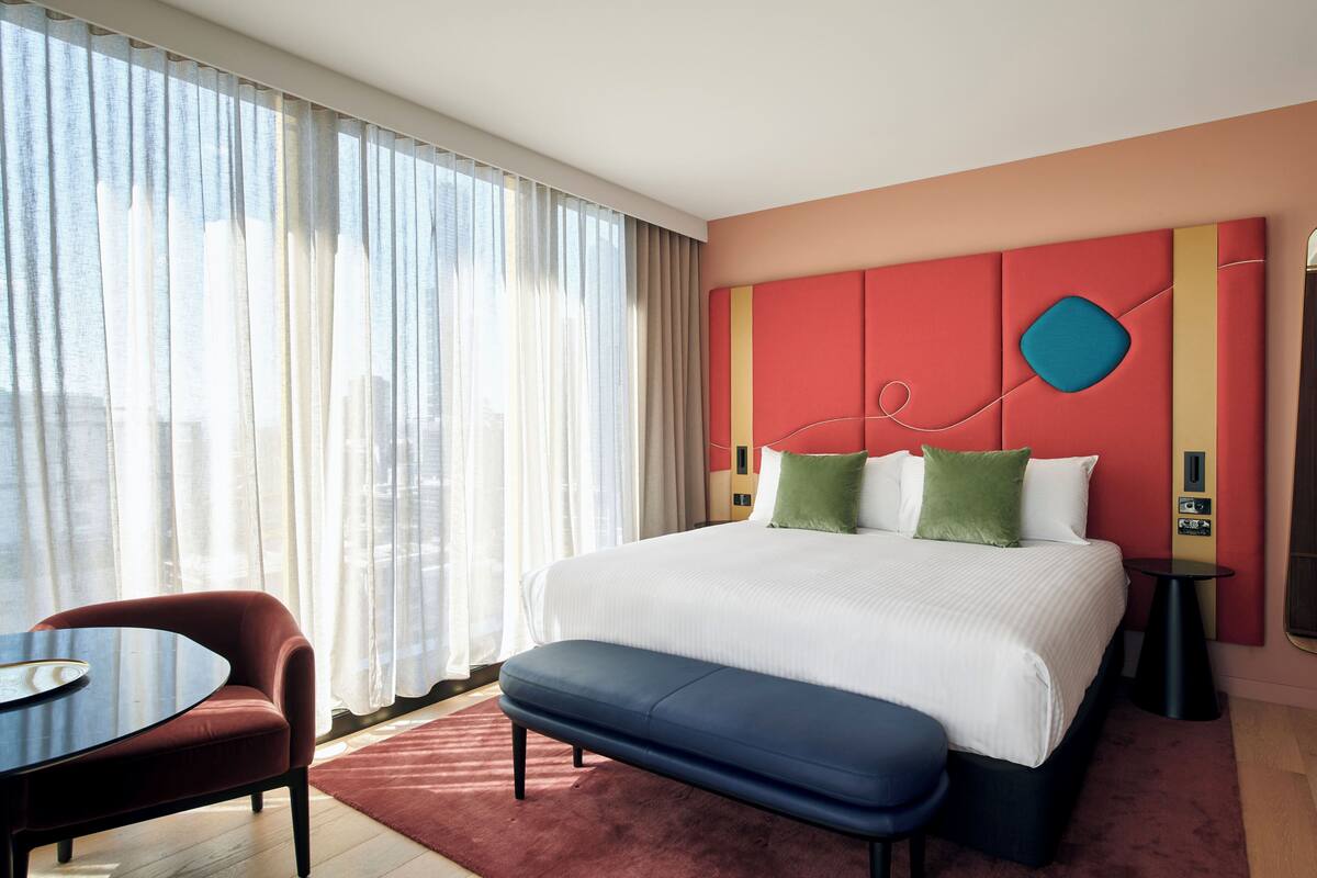 Habitación de hotel con una cama grande, un escritorio, una silla y vistas a la ciudad desde la ventana.