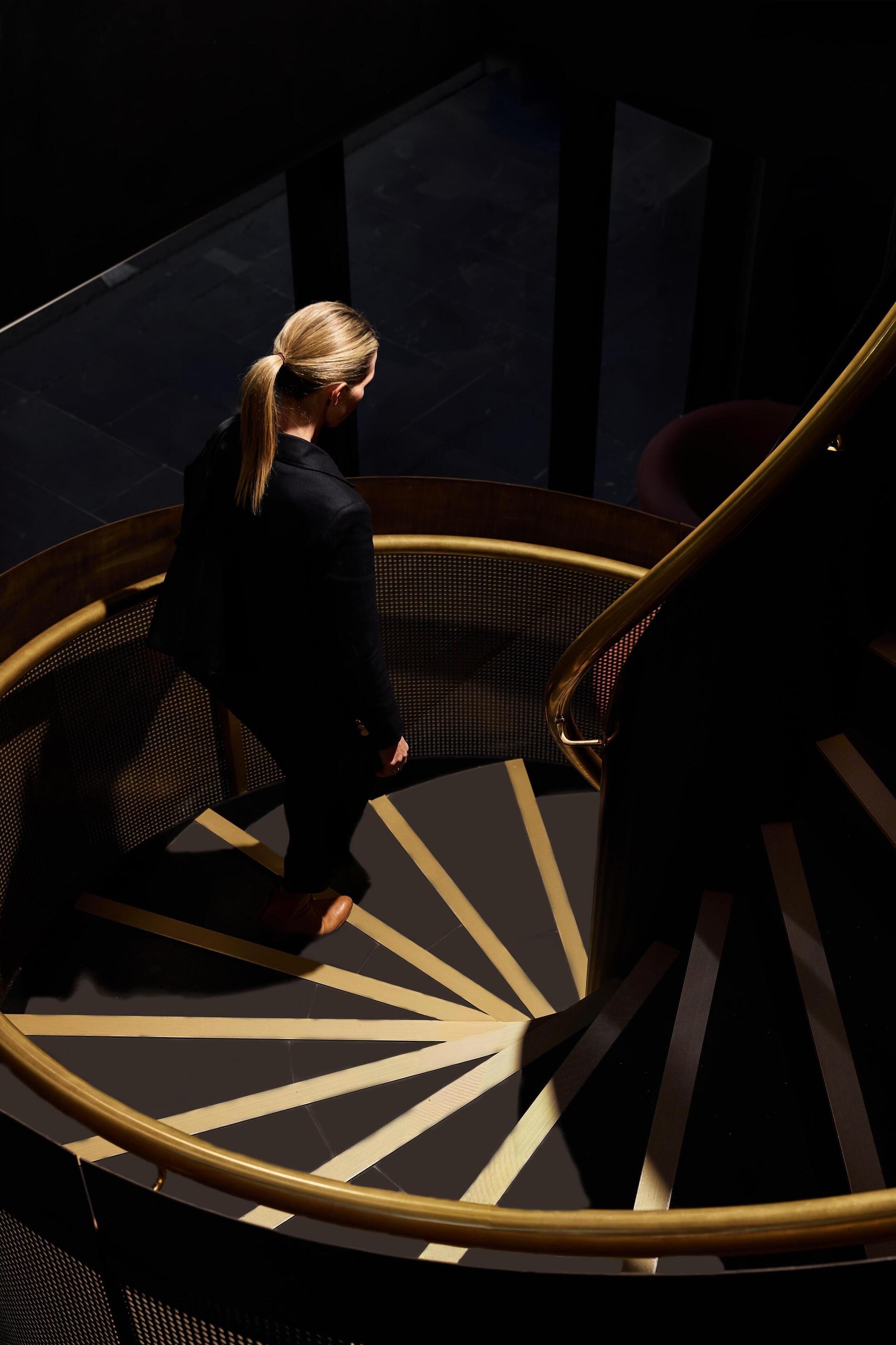 Una persona bajando una escalera espiral de interior oscuro y diseño geométrico.