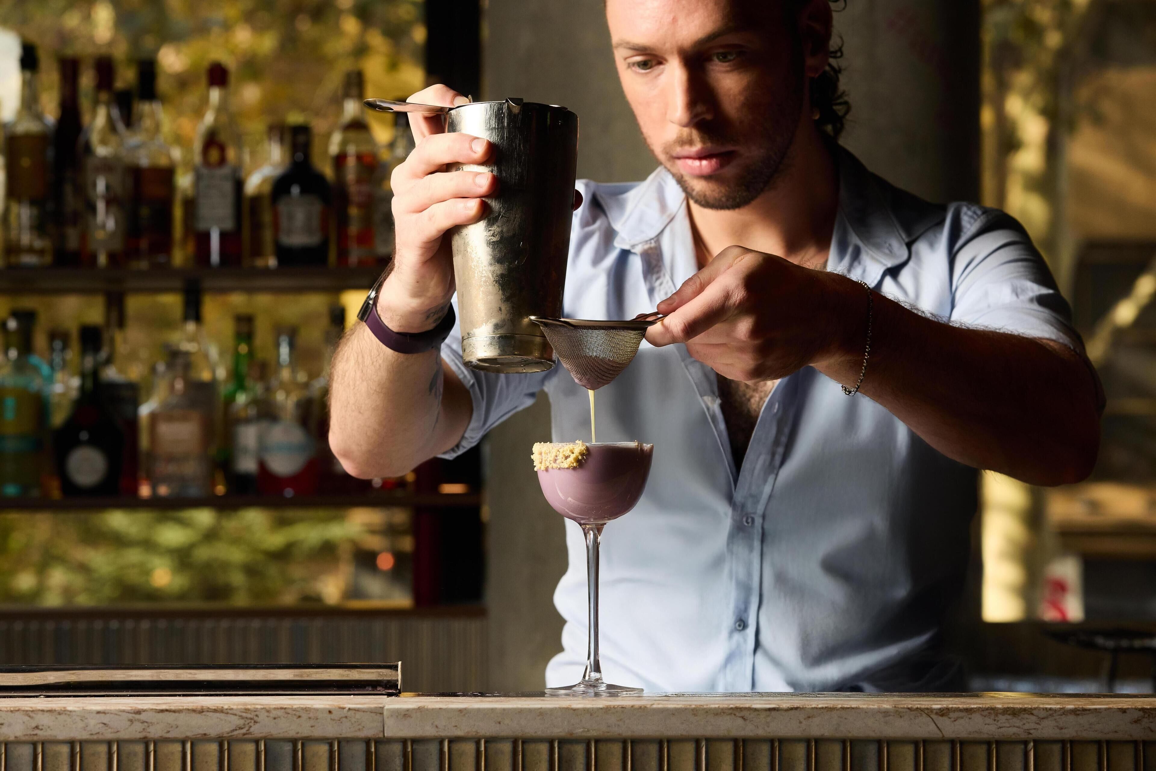 A bartender pouring a drink into a martini glass.