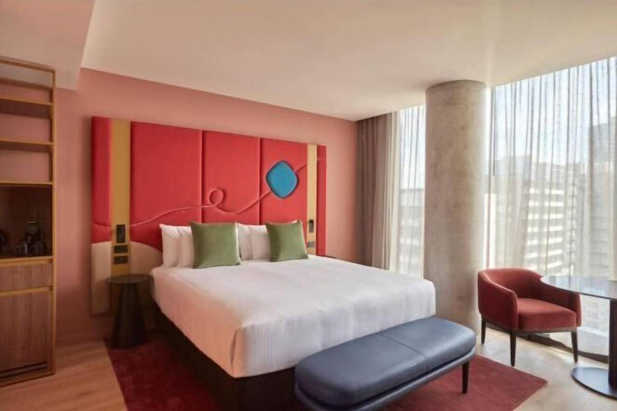 Habitación de hotel con una cama grande, un escritorio, una silla y vistas a la ciudad.
