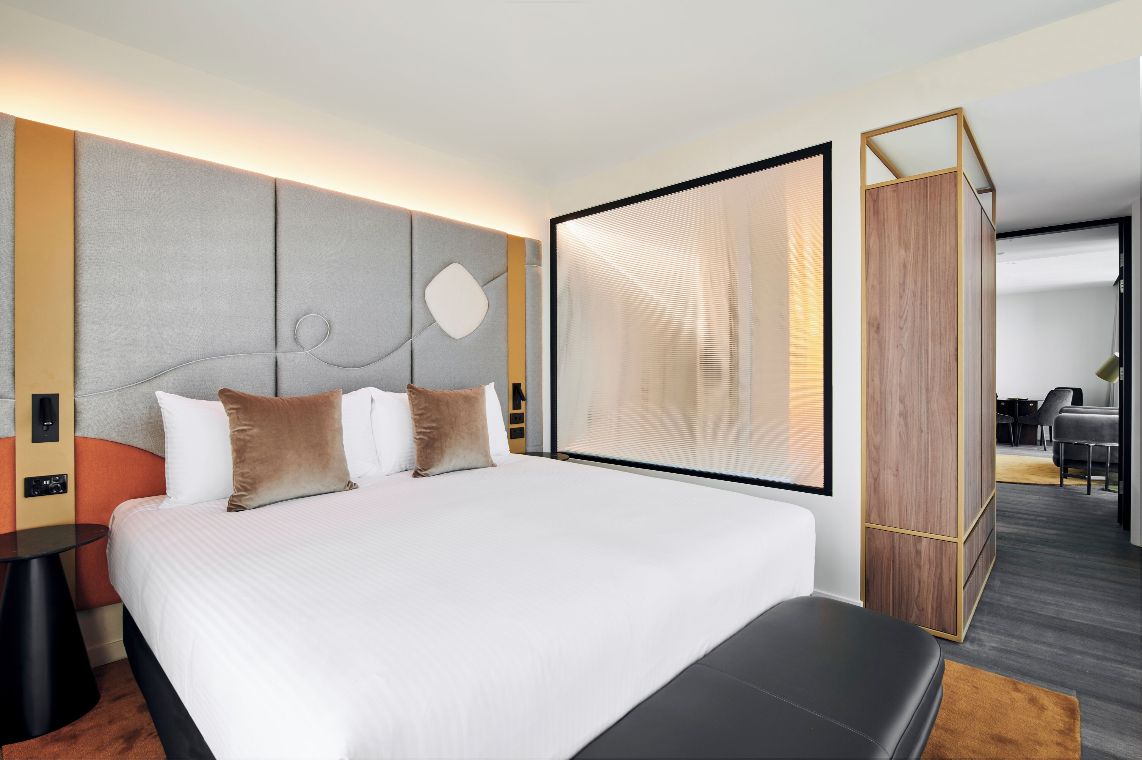 A modern hotel room with a large bed, a desk, and a view of the dining area.