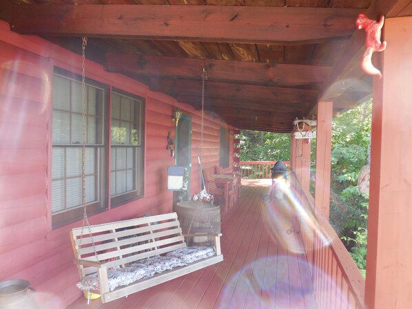 A wooden porch with a bench, a hanging bird feeder, and a swing set. - Quaint cabin with privacy and views (Maggie Valley)
