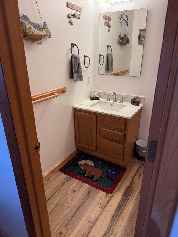 A bathroom with a wooden vanity, a sink, a mirror, and a rug with a bear design. - Quaint cabin with privacy and views (Maggie Valley)