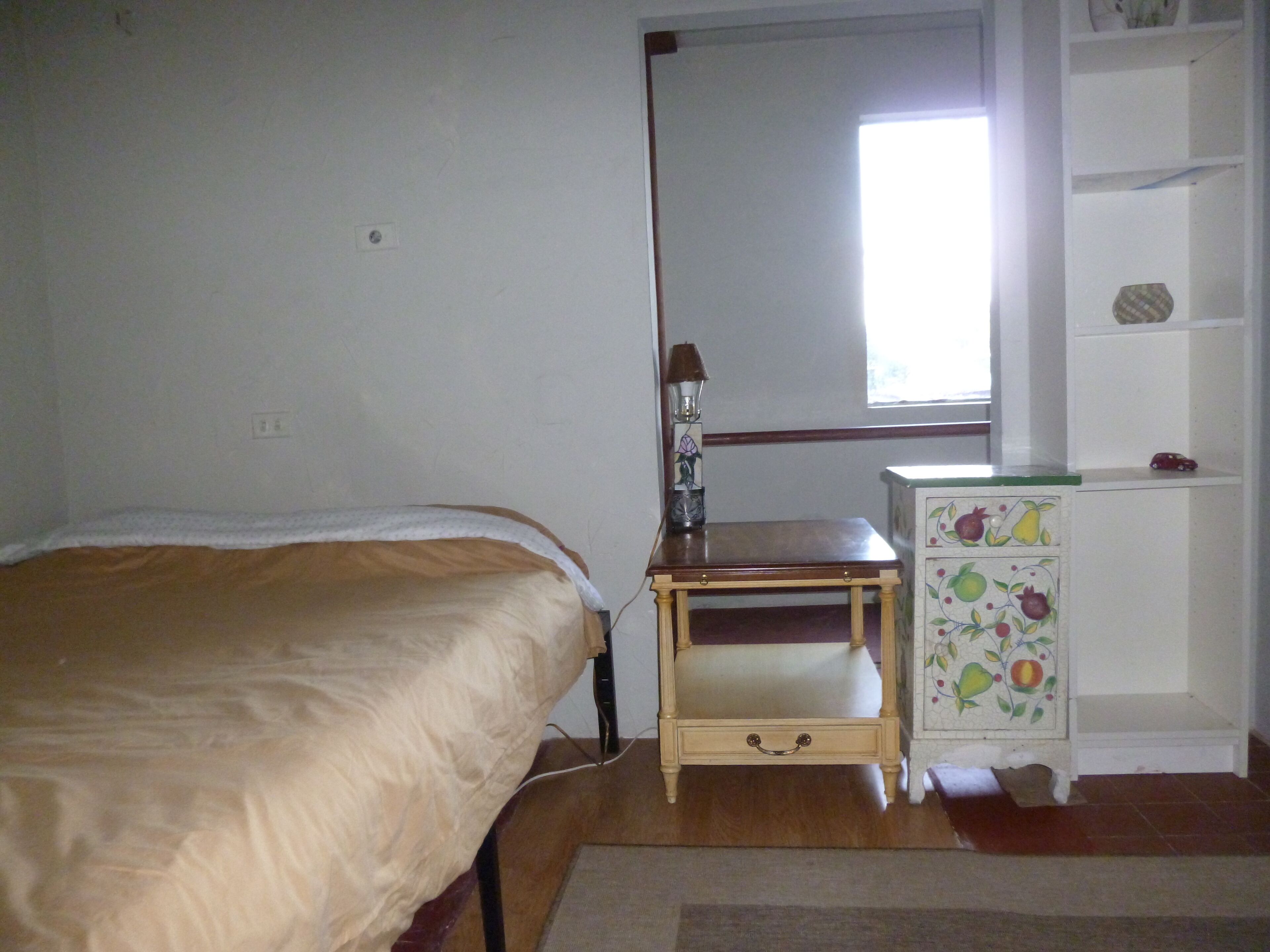 A bedroom with a bed, a nightstand with a lamp, and a small cabinet with fruit designs.