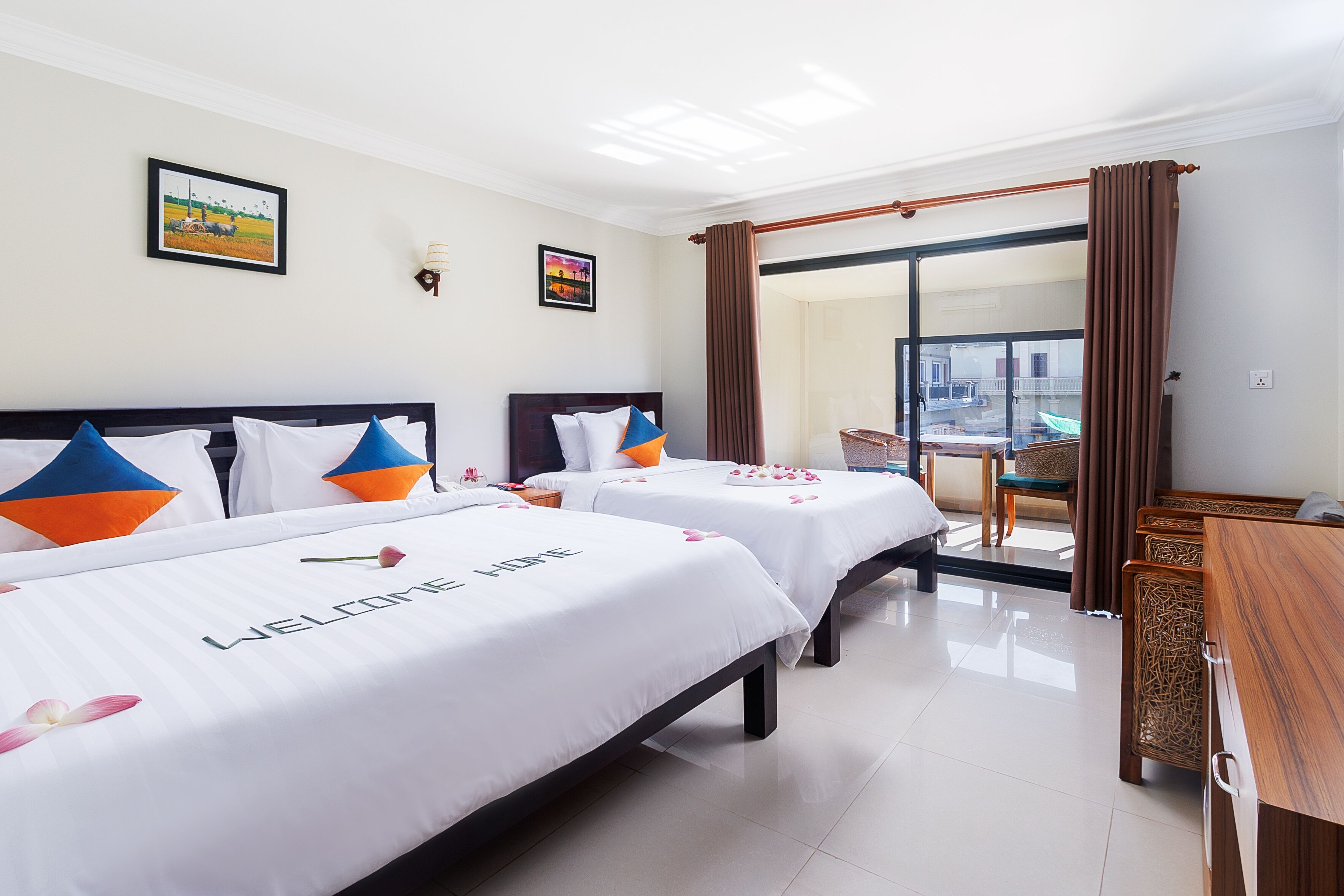 A hotel room with two beds, a wooden desk, and a balcony with a view.