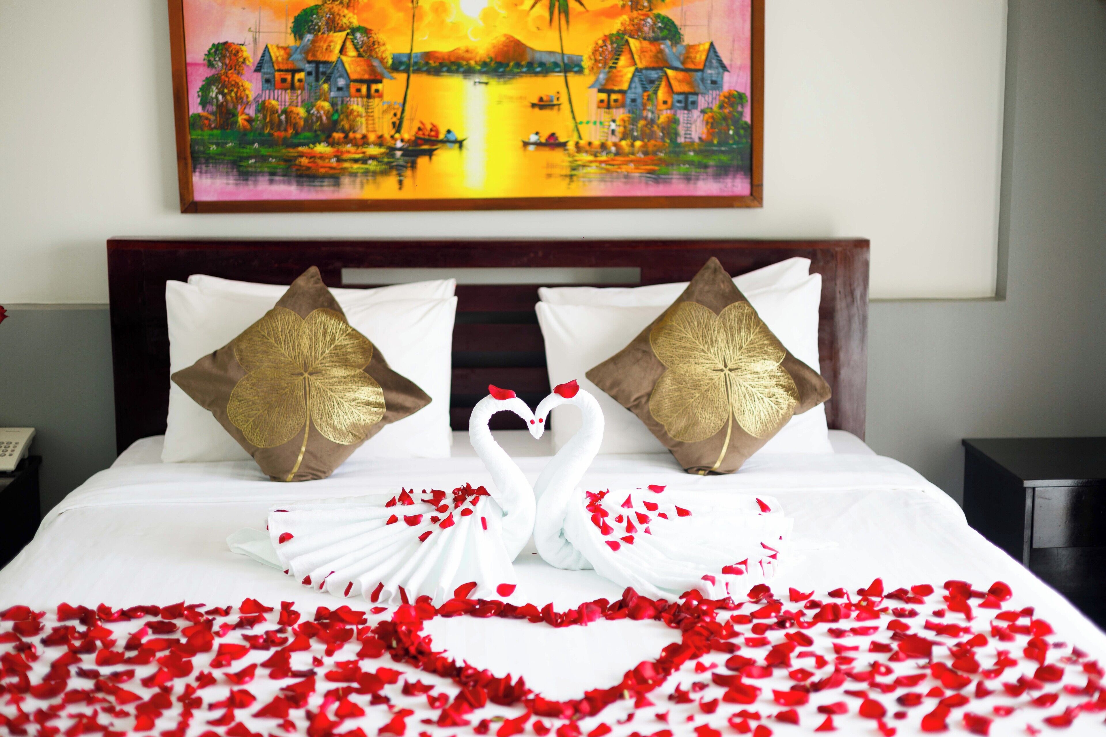 A bed with white linens, two decorative pillows, and a swan-shaped arrangement of white fabric.