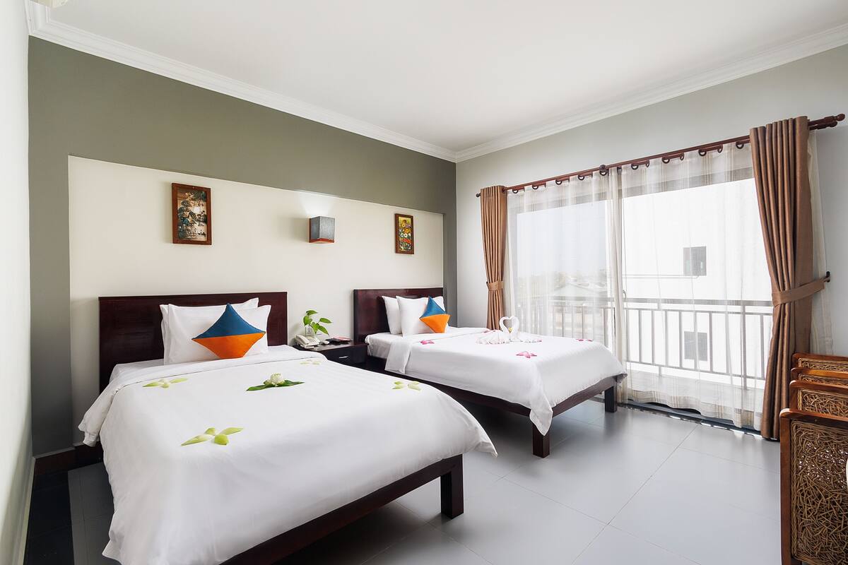A hotel room with two beds, a large window with curtains, and a view of the outside.