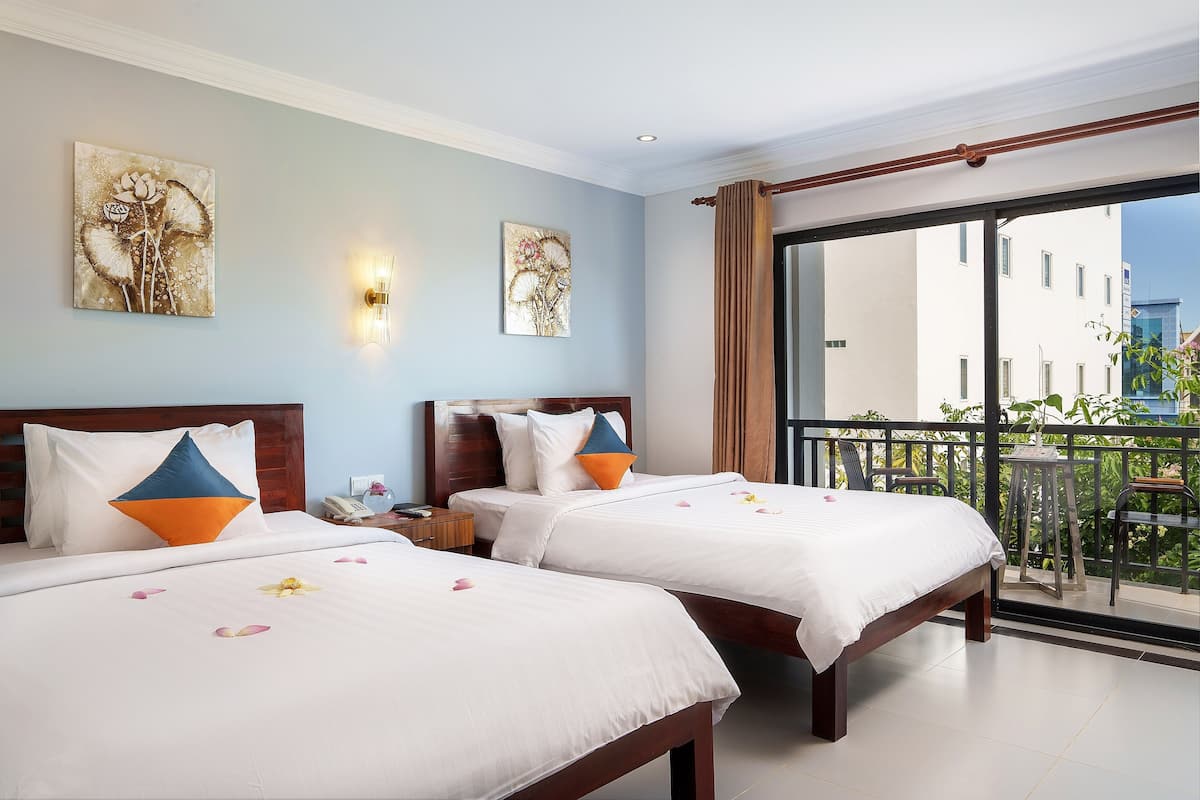 A hotel room with two beds, a balcony with a table and chairs, and artwork on the walls.