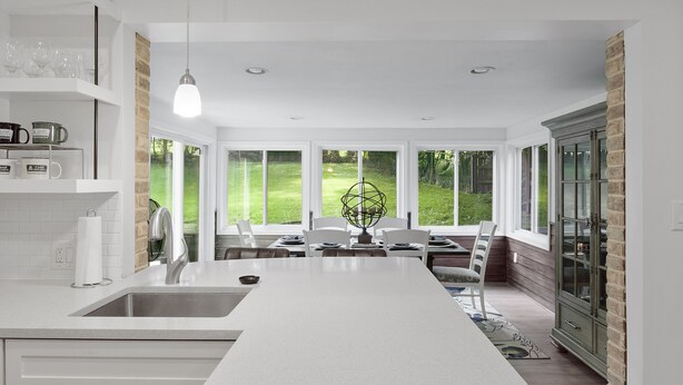 A modern kitchen with a central island, large windows, and a dining area with a view of the outdoors.