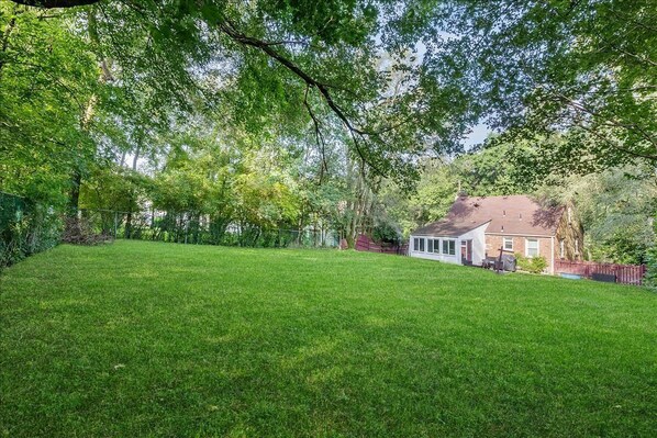 A spacious backyard with a house, a lawn, and a wooden fence.