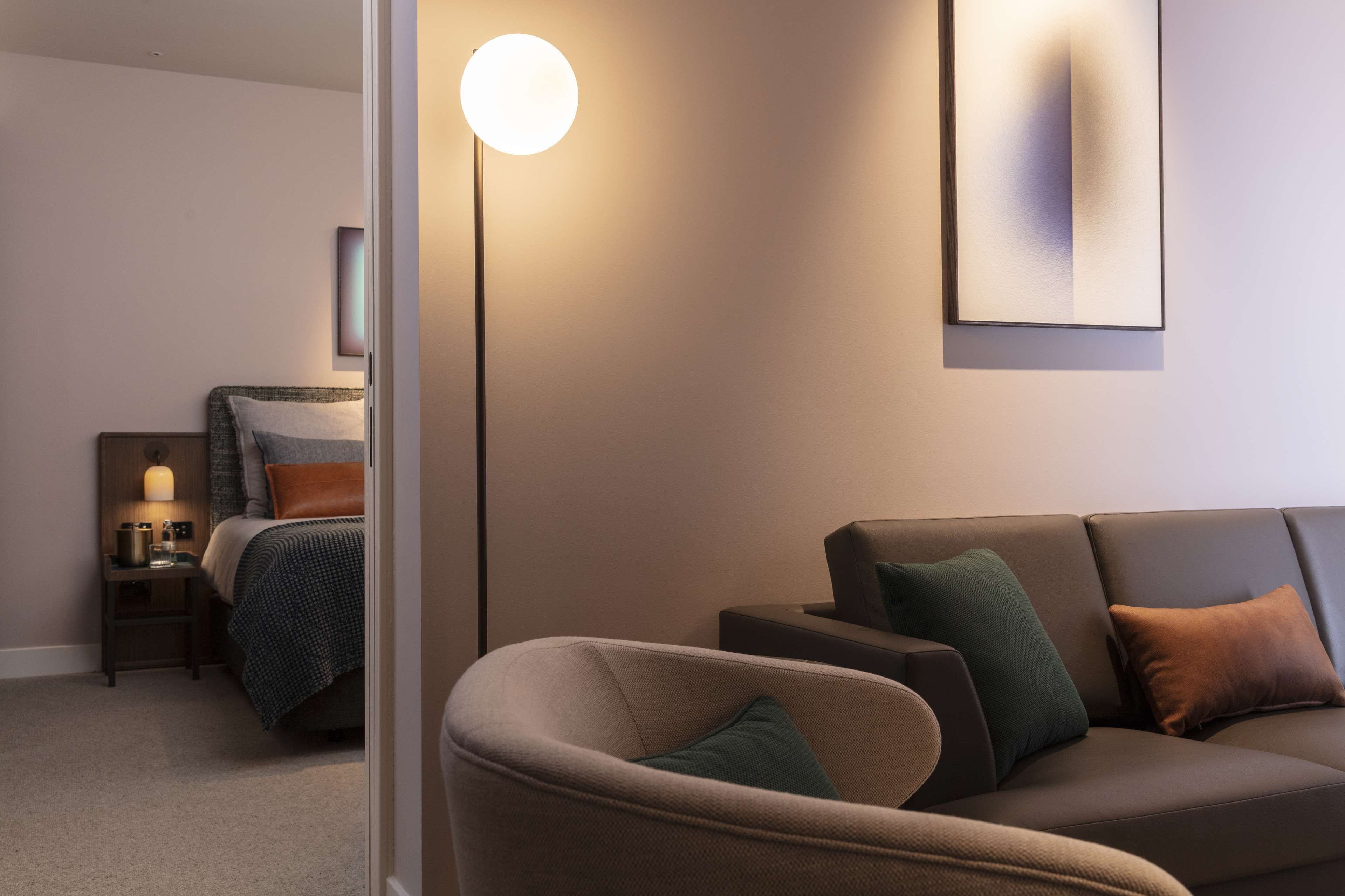 Une chambre d’hôtel moderne équipée d’un lit, d’une table de chevet, d’une lampe, d’un canapé et d’un lampadaire.