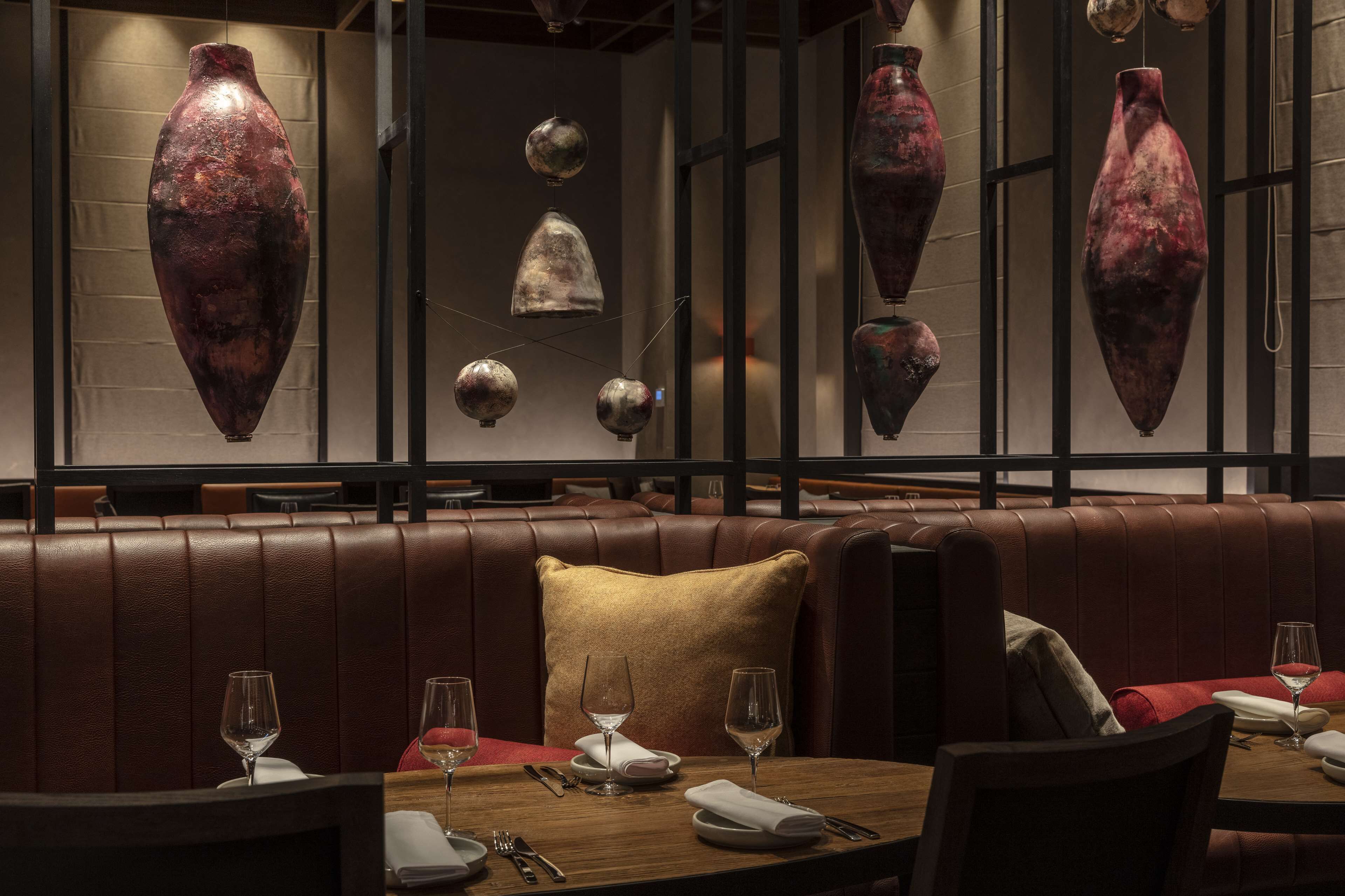 A restaurant interior with leather booths, hanging vases, and neatly set dining tables.