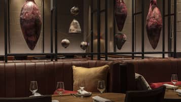 A restaurant interior with leather booths, hanging vases, and neatly set dining tables.