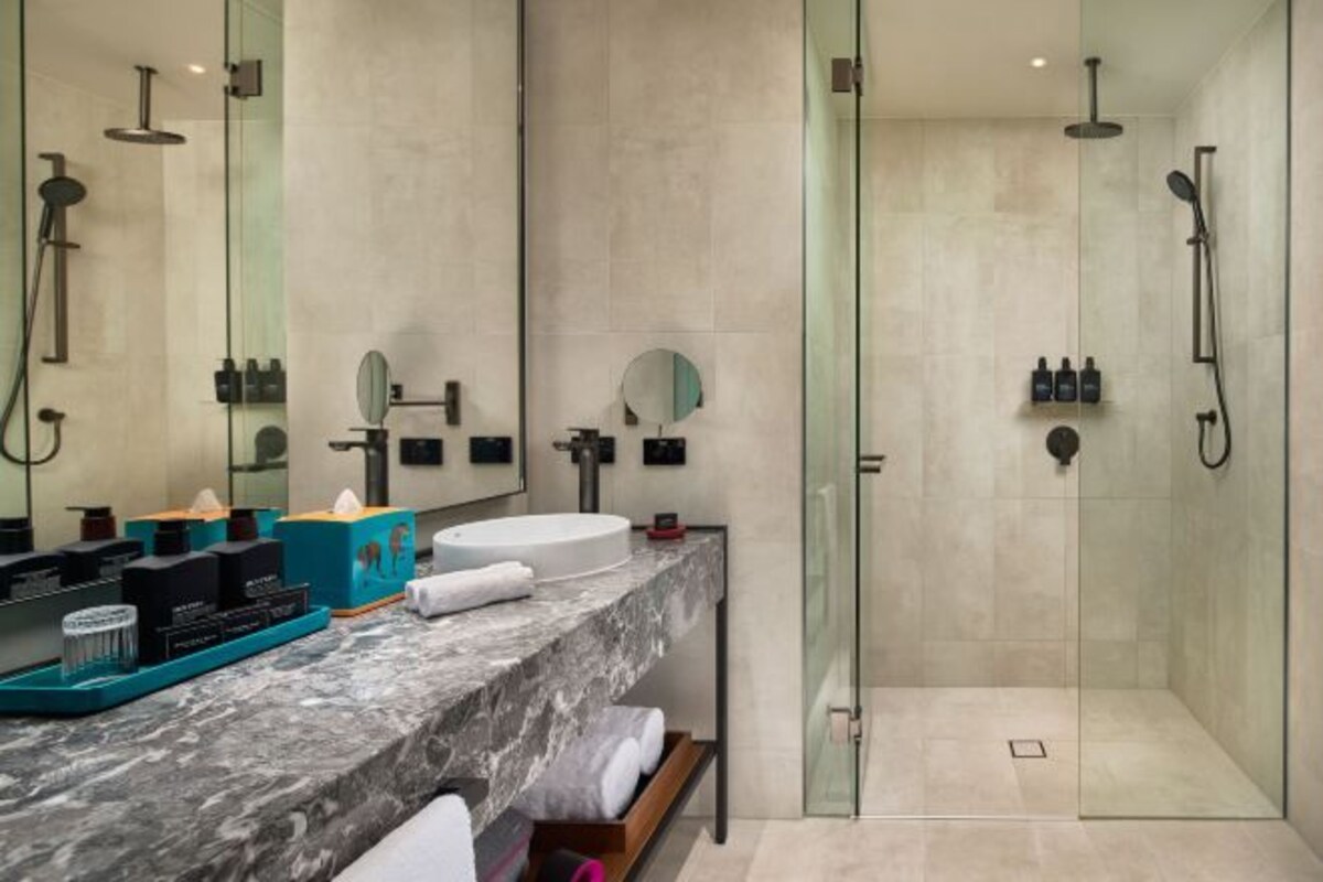 Un baño moderno con lavamanos de mármol, cabina de ducha con vidrio y tocador con artículos de aseo.