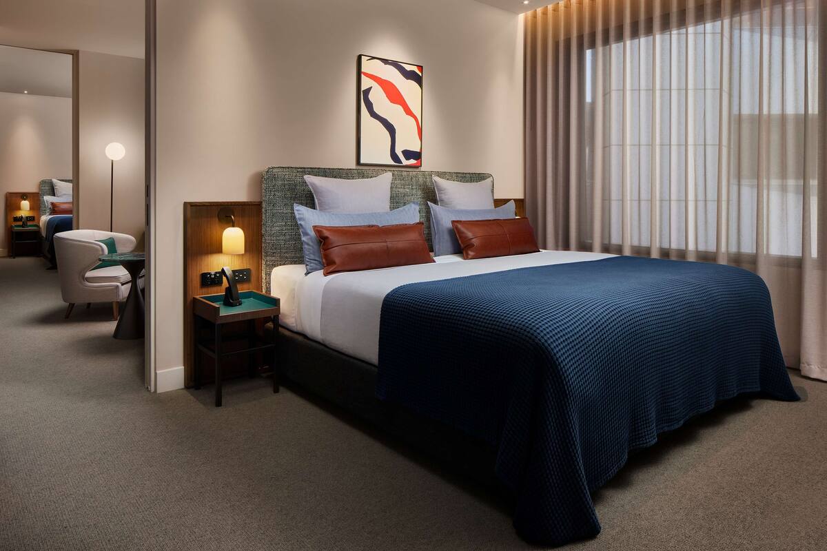 A hotel room with a large bed, a bedside table with a lamp, a chair, and a mirror.