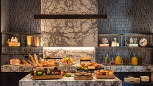 A marble counter with various food items and a selection of books and decorative items on shelves. - Next Hotel Melbourne, Curio Collection by Hilton (Melbourne)