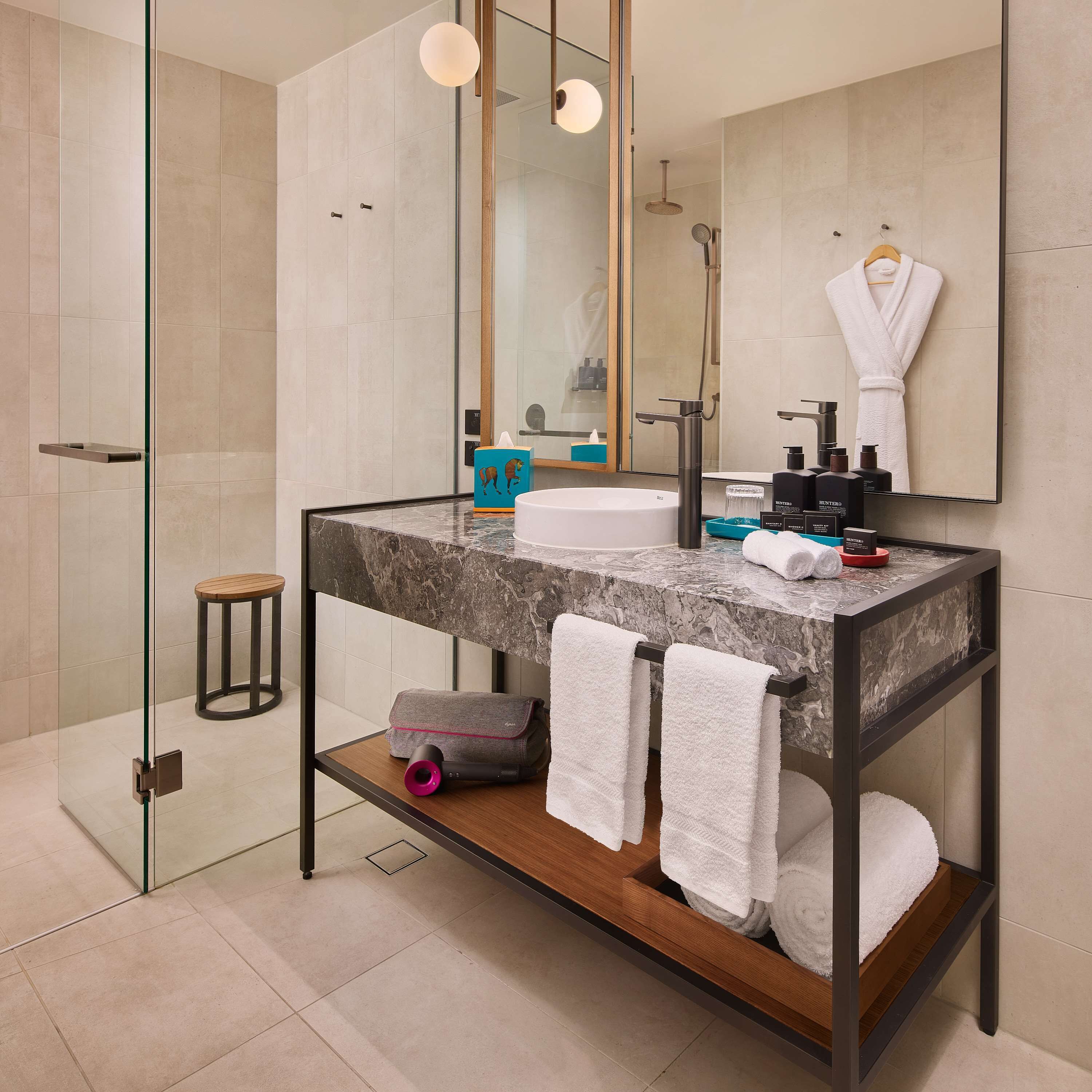 Un baño moderno con lavamanos de mármol, cabina de ducha de vidrio y tocador de madera.