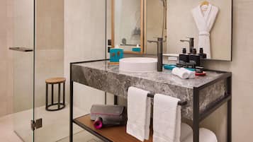 Un baño moderno con lavamanos de mármol, cabina de ducha de vidrio y tocador de madera.