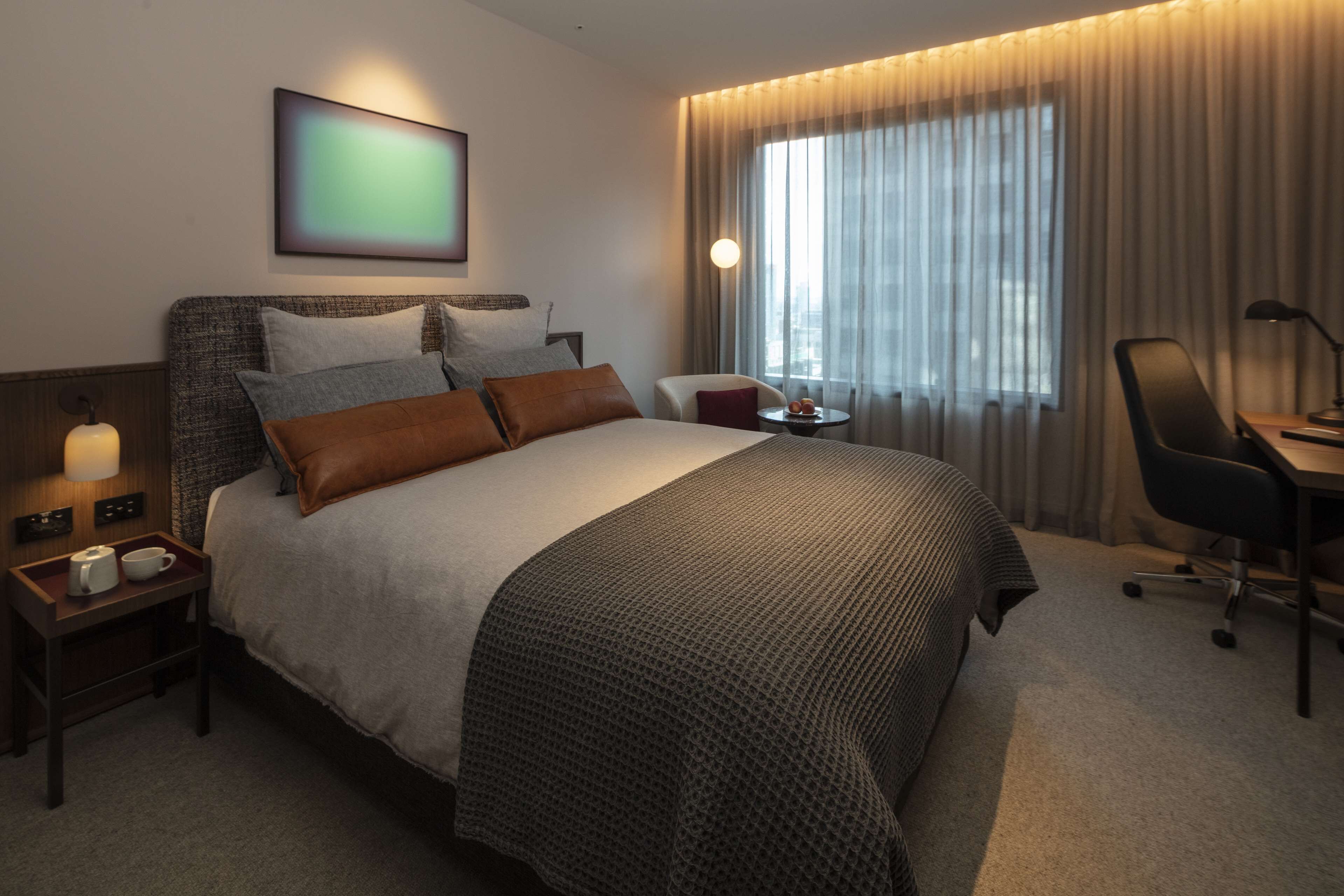 A hotel room with a large bed, a bedside table with a lamp, a chair, and a desk.