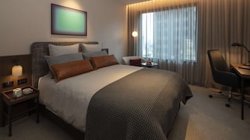 A hotel room with a large bed, a bedside table with a lamp, a chair, and a desk.