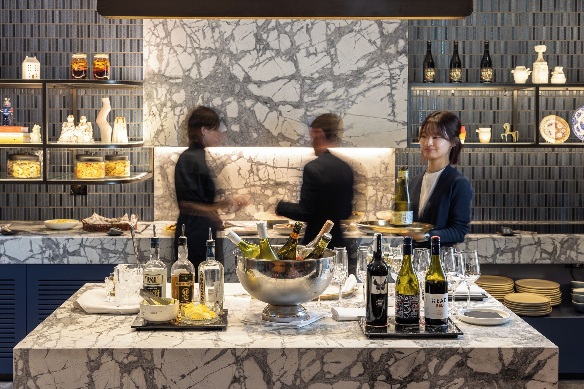 A bar area with marble countertops, bottles of wine, and a large metal bowl.