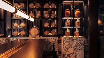 A bar area with a marble countertop, wooden barrels, and shelves with glassware.