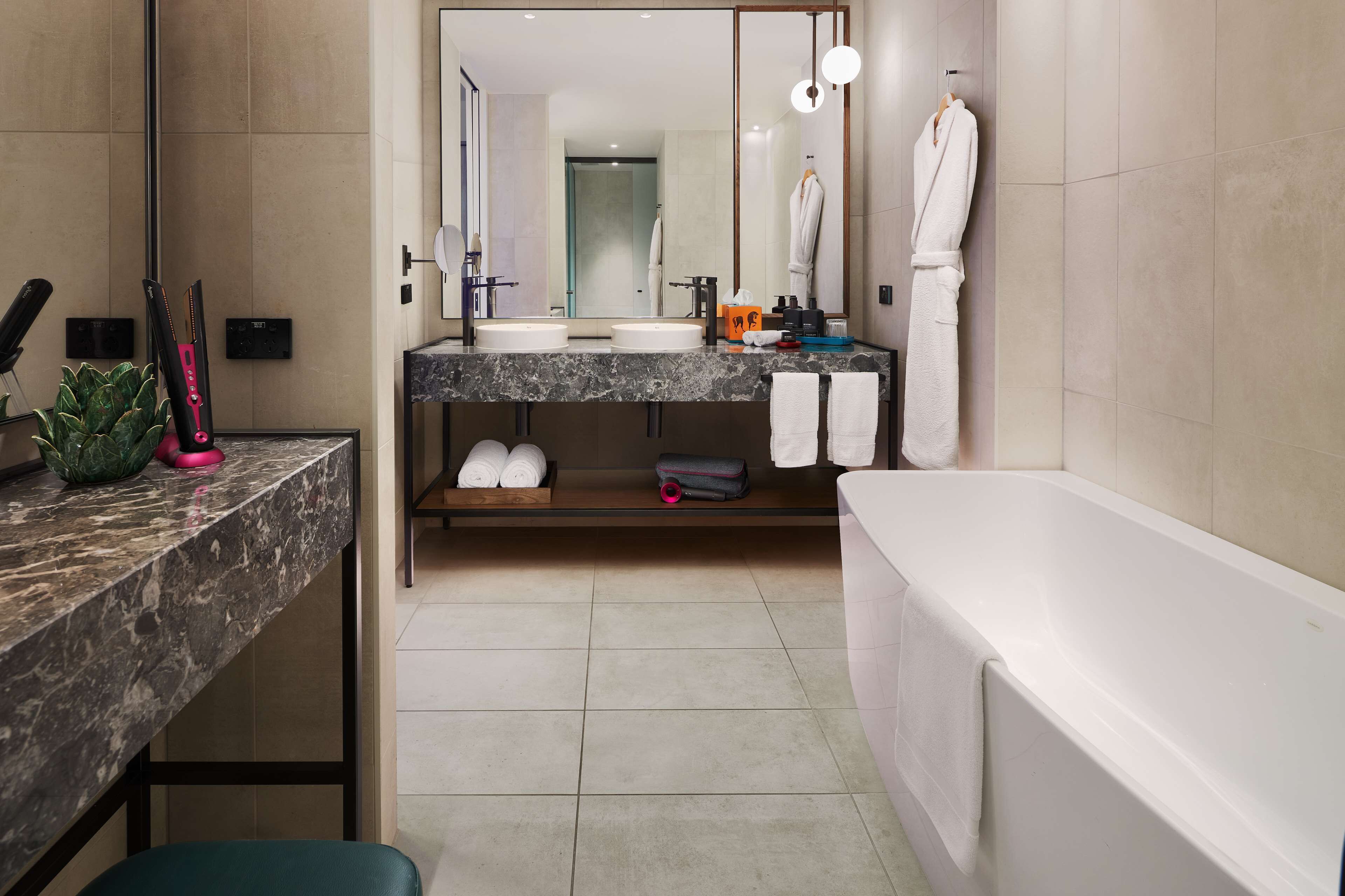 Une salle de bain moderne dotée d’un grand miroir, de deux vasques, d’une baignoire et d’un meuble-lavabo avec un plan de travail en marbre.