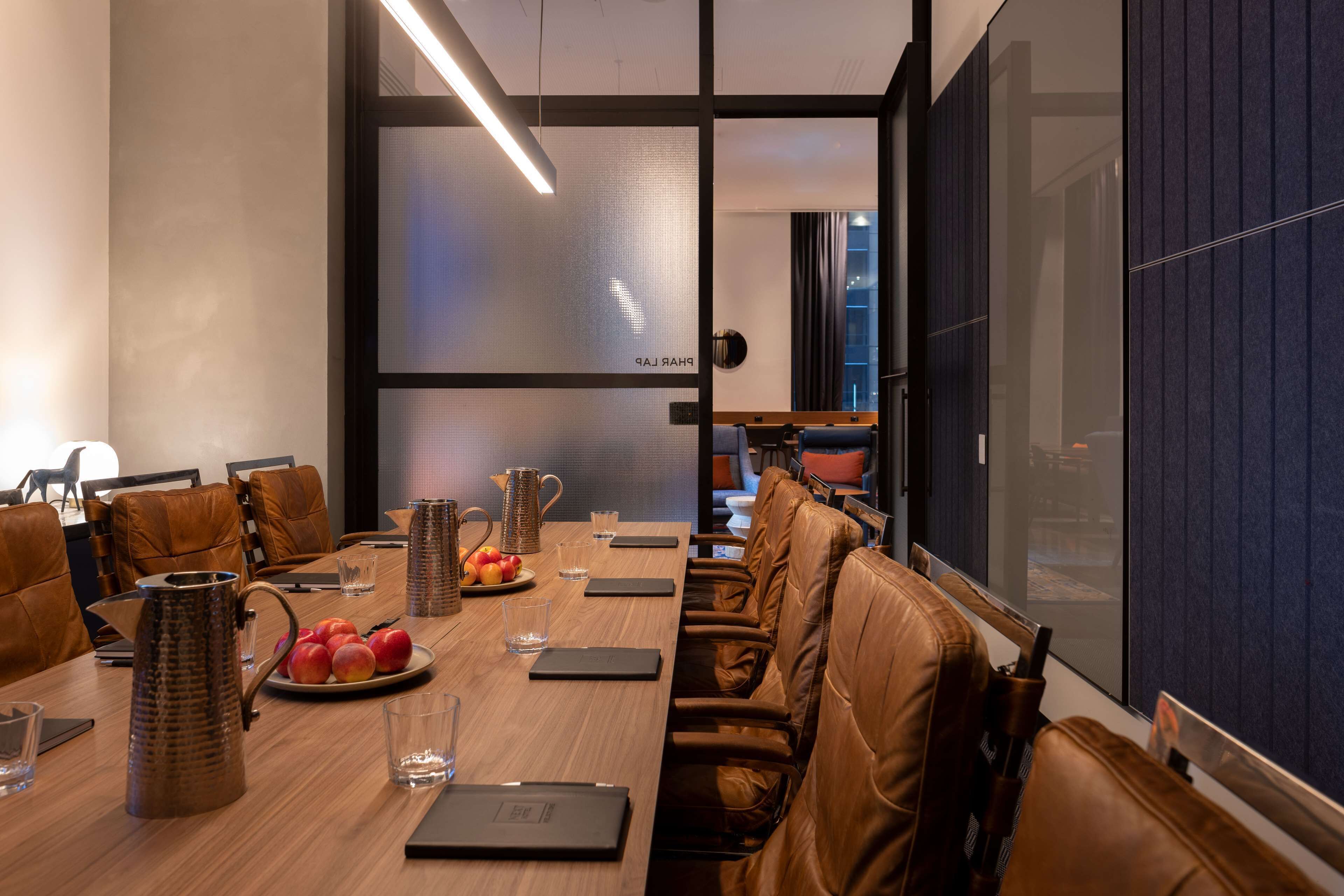 A modern meeting room with a wooden table, leather chairs, and a glass partition.