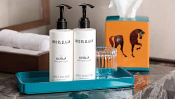 Two bottles of Who is Elijah Nightcap body wash and lotion, a tissue box, and a glass of water on a blue tray.