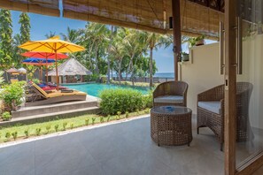 Un balcón con vista a una piscina, sillones de descanso y sombrillas.