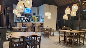 Un restaurante con mesas y sillas de madera, lámparas de mimbre colgantes y una zona de bar con una pantalla de televisión.