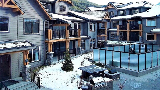 Un edificio moderno de varios pisos con un área exterior cubierta y una piscina con cerramientos de vidrio.