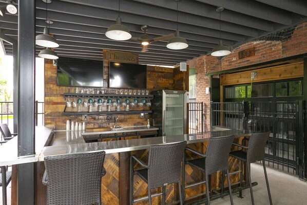 A bar area with a long counter, multiple stools, and a refrigerator.