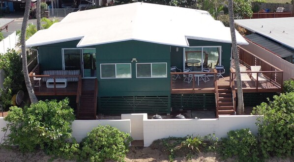 Una casa de dos plantas con fachada verde, una terraza con mobiliario exterior y un ventanal grande en el piso superior.