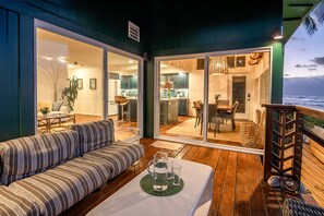 Un área de estar exterior acogedora con sofá y mesa, una cocina visible a través de puertas de vidrio y vistas al océano.
