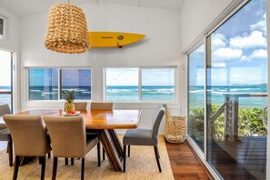 Un comedor con una mesa y sillas de madera, una lámpara colgante de fibras tejidas y una tabla de surf en la pared.